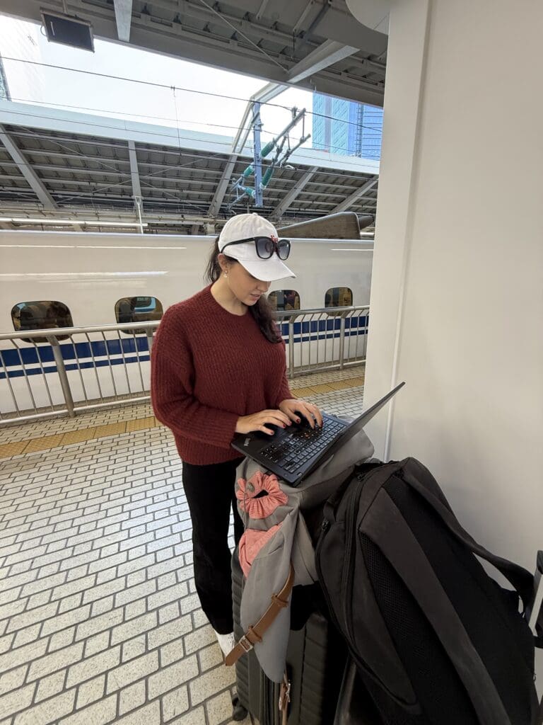 Luxury Travel Advisor Alexis Berlin planning client vacations on a laptop balanced on top of a suitcase while waiting to board a train in Japan
