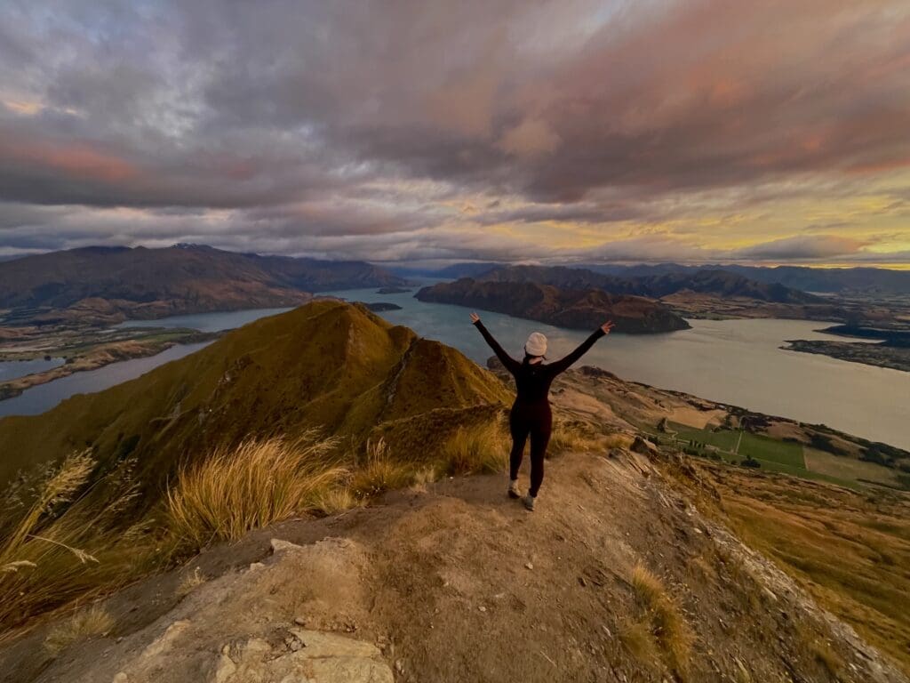Luxury Travel Advisor Alexis Berlin stands at Roy's Peak under a beautiful sunrise